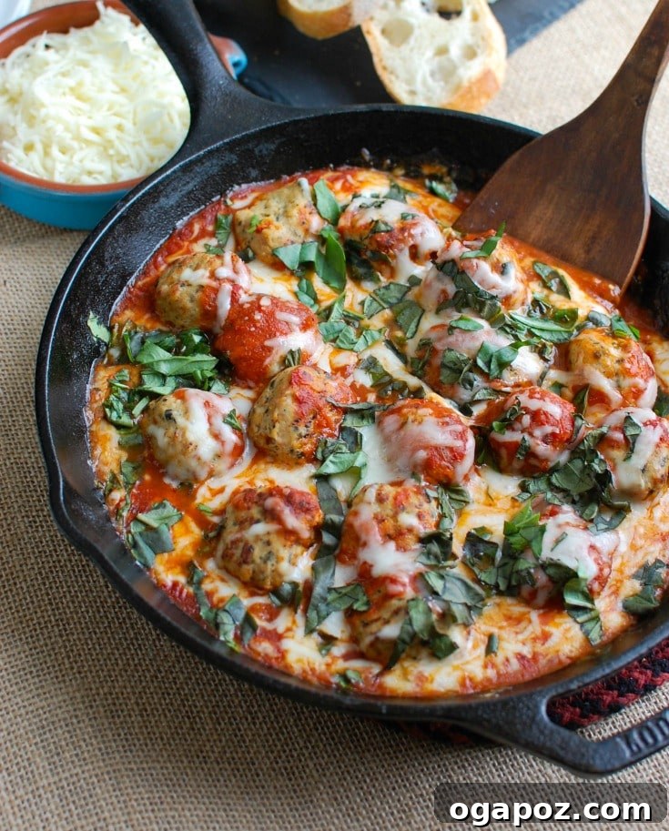 A warm cast iron skillet filled with bubbling Skillet Tomato Basil Meatballs, generously topped with melted mozzarella and fresh green basil leaves.
