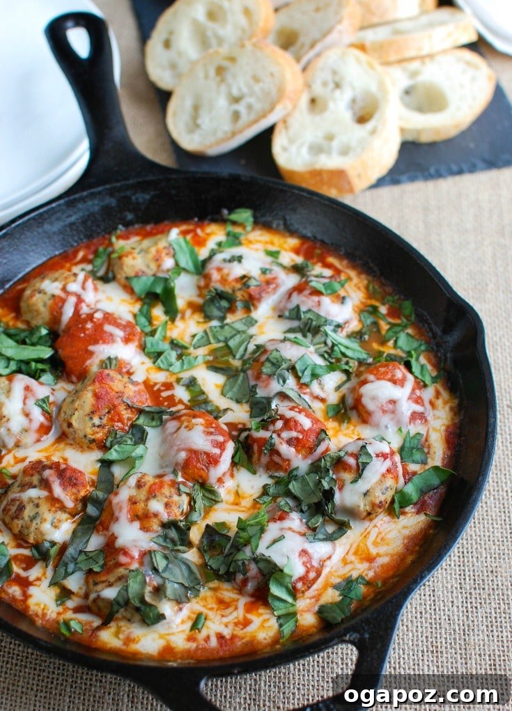 Close-up view of Skillet Tomato Basil Meatballs baking in an oven-safe dish, with mozzarella cheese melting and bubbling beautifully.