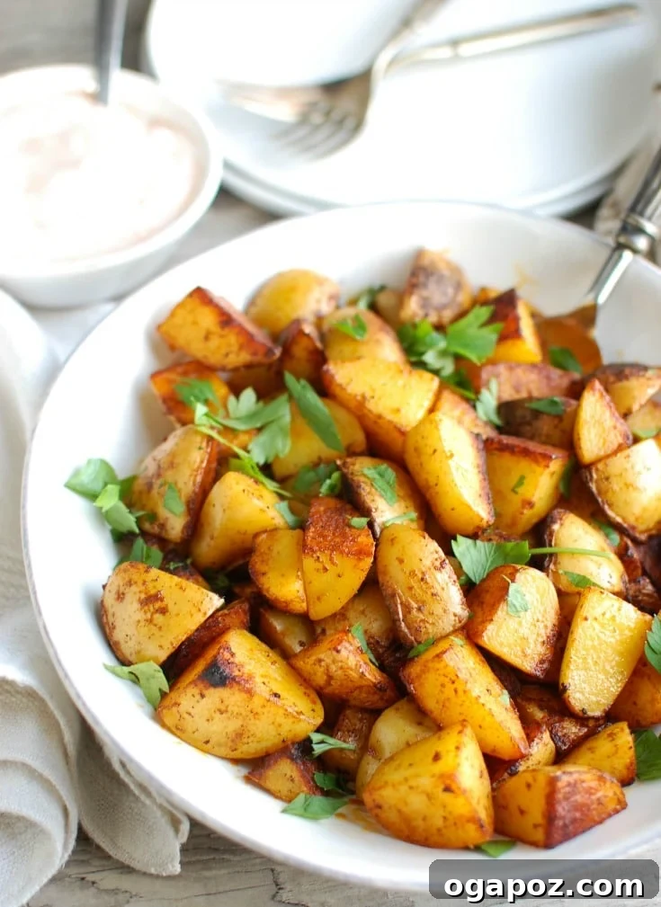 Smoky Paprika Potatoes with Cooling Spiced Yogurt 2 Crispy Paprika Roasted Potatoes with Spiced Yogurt Sauce ready to be served, showcasing their golden-brown edges and a vibrant green parsley garnish. A bowl of creamy spiced yogurt dip sits beside them.