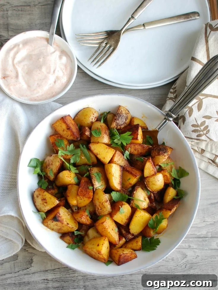 Smoky Paprika Potatoes with Cooling Spiced Yogurt 4 Overhead shot of Paprika Roasted Potatoes generously garnished with fresh parsley, served alongside a bowl of Spiced Yogurt Sauce, highlighting the vibrant colors and inviting presentation.