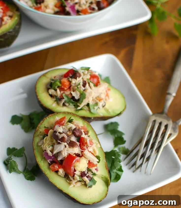 Zesty Mexican Tuna Avocado Boats 3 Mexican Tuna Stuffed Avocados combines tuna, black beans, fresh vegetables, lime juice and spices to create a healthy and easy snack or lunch that is also heart healthy, shown on a rustic wooden board.