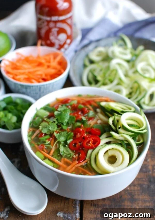 Fiery Fowl Broth 4 A close-up shot of a spoonful of Spicy Chicken Soup, highlighting the chicken, carrots, and zucchini noodles, with garnishes in the background.