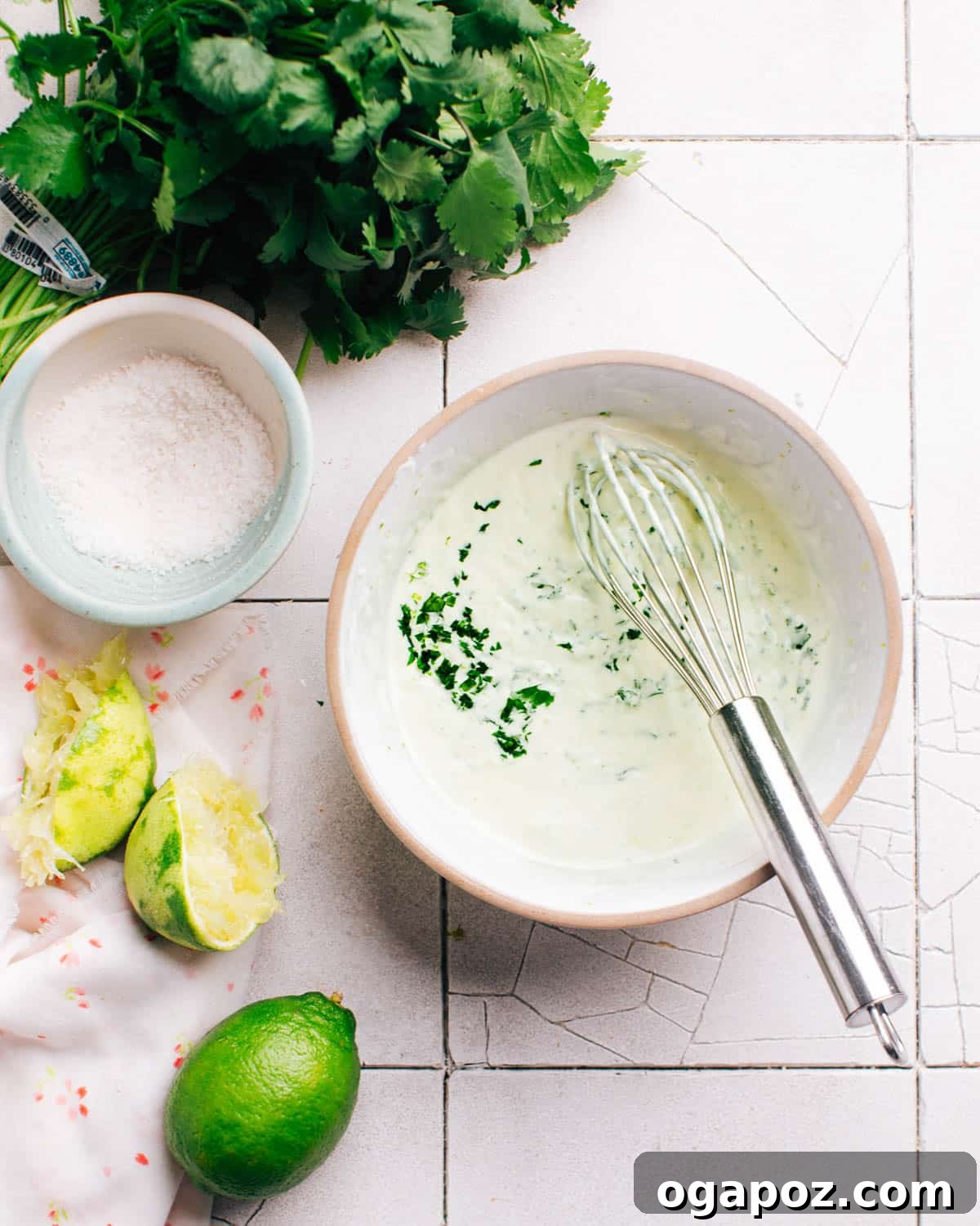 Vibrant Cilantro-Lime Drizzle 2 Freshly made cilantro lime crema in a small bowl with a whisk. Limes, kosher salt, and cilantro are placed nearby, highlighting the fresh ingredients.