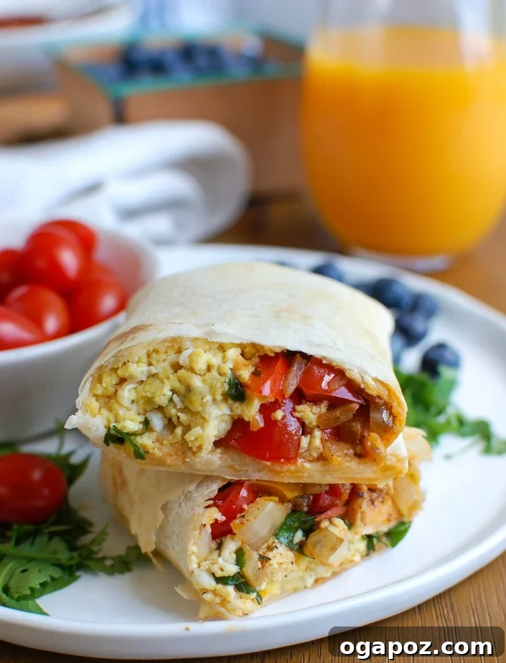 A half-rolled vegetarian breakfast egg burrito on a cutting board, showing the vibrant filling of scrambled eggs, peppers, cheese, and a garnish of cherry tomatoes.