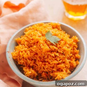 A serving of Instant Pot Mexican rice is presented in a bowl, adorned with a sprinkle of fresh cilantro. Adjacent to the bowl, a kitchen cloth and two glasses can be seen.