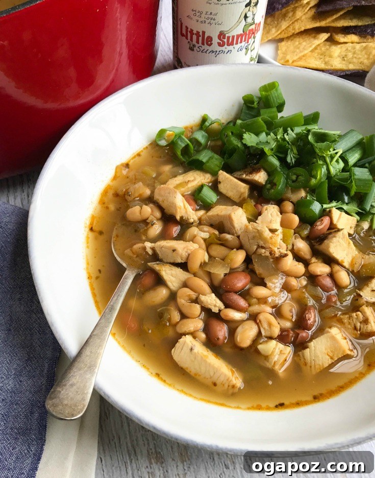 Close-up shot of Green Chicken Chili simmering in a pot, showing beans, chicken, and green chiles.