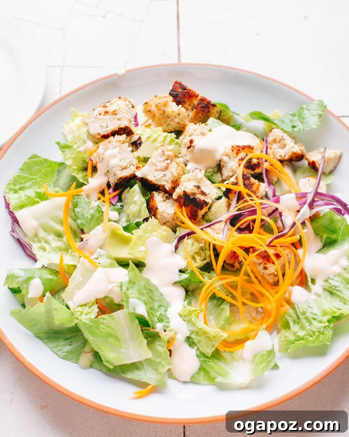 Irresistibly Juicy Ground Chicken Burgers 7 A cooked ground chicken burger patty is sliced and arranged on a fresh, vibrant salad with various greens, carrots, onions, and a creamy dressing.
