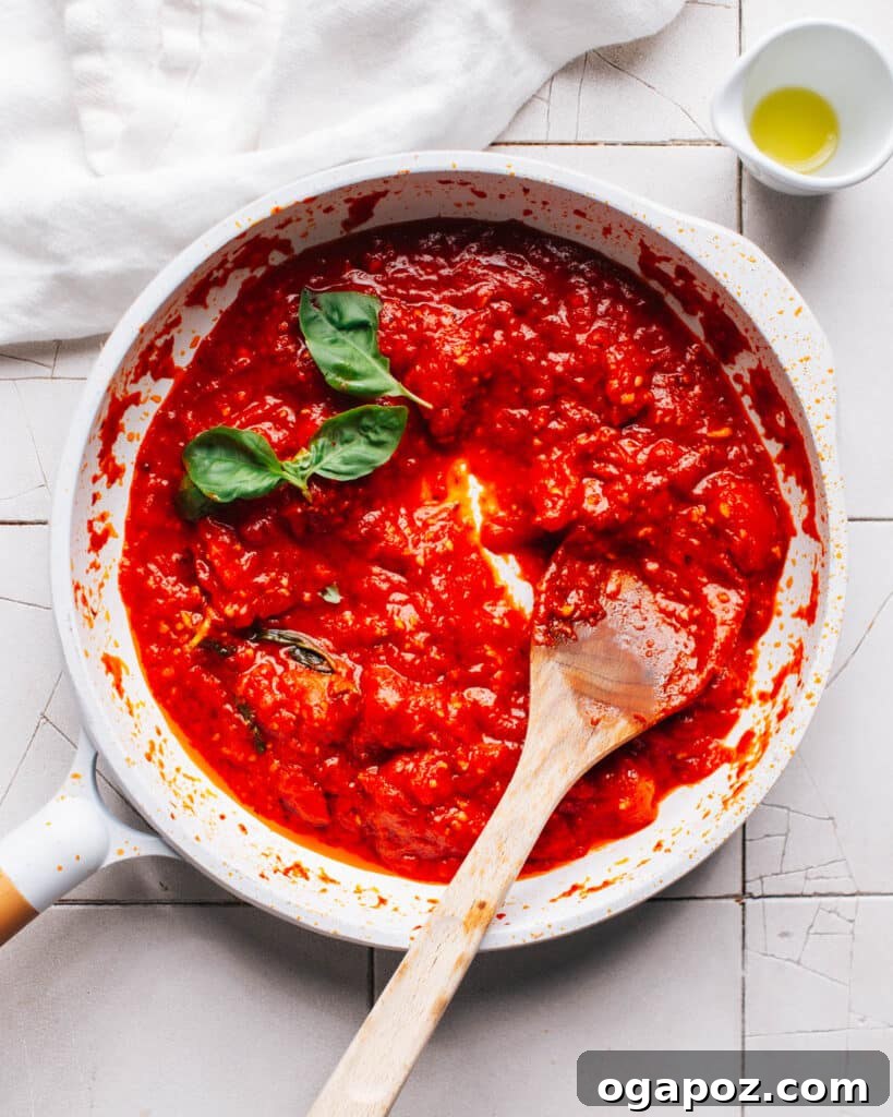 The Best Homemade Pizza Sauce You'll Ever Make 2 Homemade Pizza Sauce simmering in a pan with a wooden spoon, rich red color.