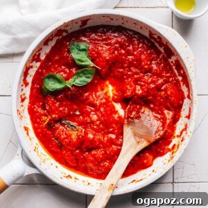 The Best Homemade Pizza Sauce You'll Ever Make 12 Homemade Pizza Sauce simmering in a pan with a wooden spoon.
