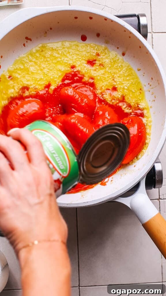 The Best Homemade Pizza Sauce You'll Ever Make 6 Chopped tomatoes being added to the saucepan with sautéed garlic and herbs for pizza sauce.
