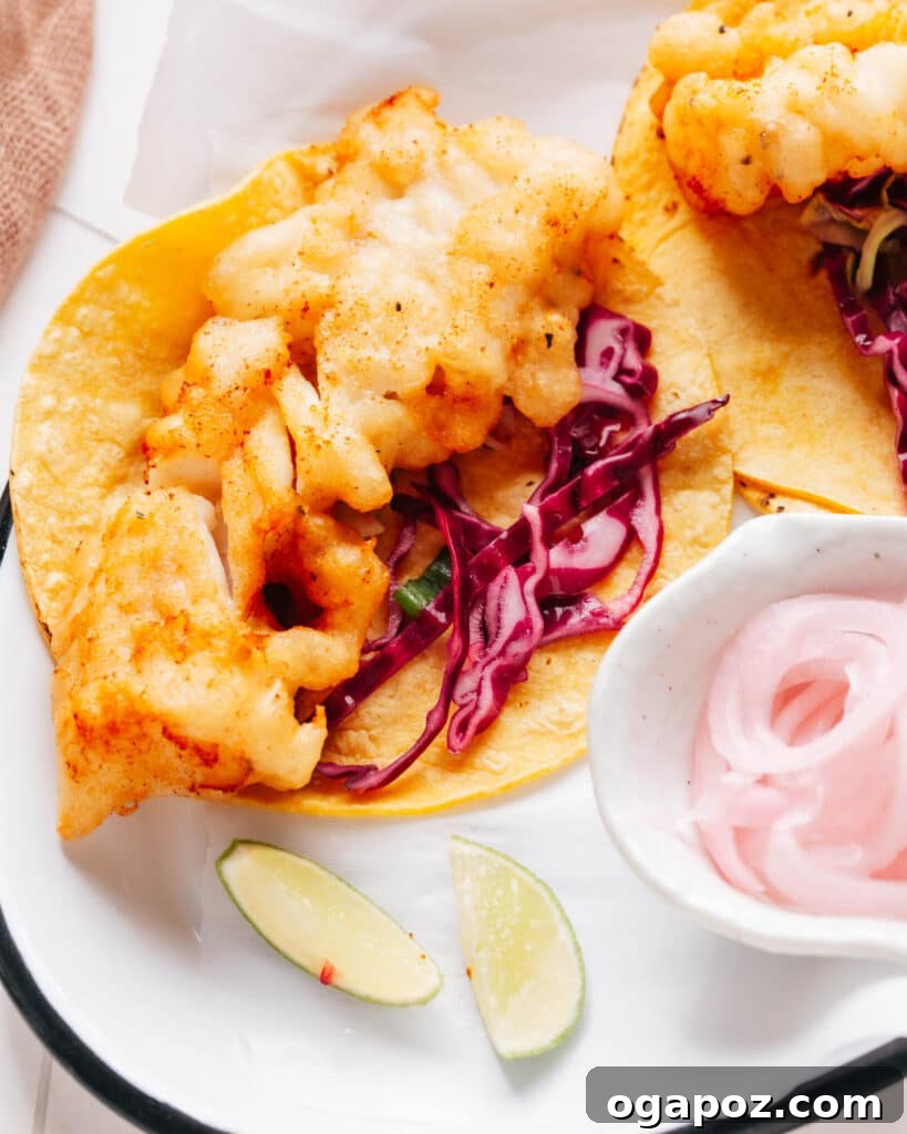 Zesty Fish Taco Slaw 5 A close-up of beautifully assembled fish tacos, generously loaded with flaky fish, vibrant cabbage slaw, and a drizzle of creamy sauce, served with fresh lemon wedges.