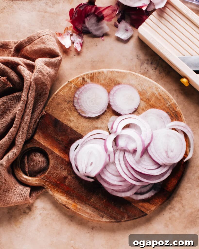 Instant 5-Minute Pickled Onions 6 A thinly sliced red onion on a wooden chopping board with a mandoline slicer nearby, illustrating the importance of precise slicing for pickling.
