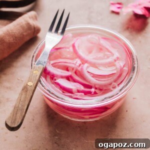 Close-up of vibrant pink pickled onions in a small glass dish with a fork, ready to be served.
