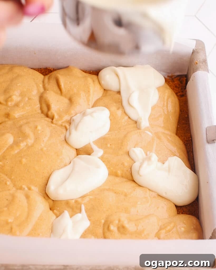 A knife gently swirling vanilla and pumpkin cheesecake batters together on a graham cracker crust in a baking pan, creating a beautiful marbled effect.