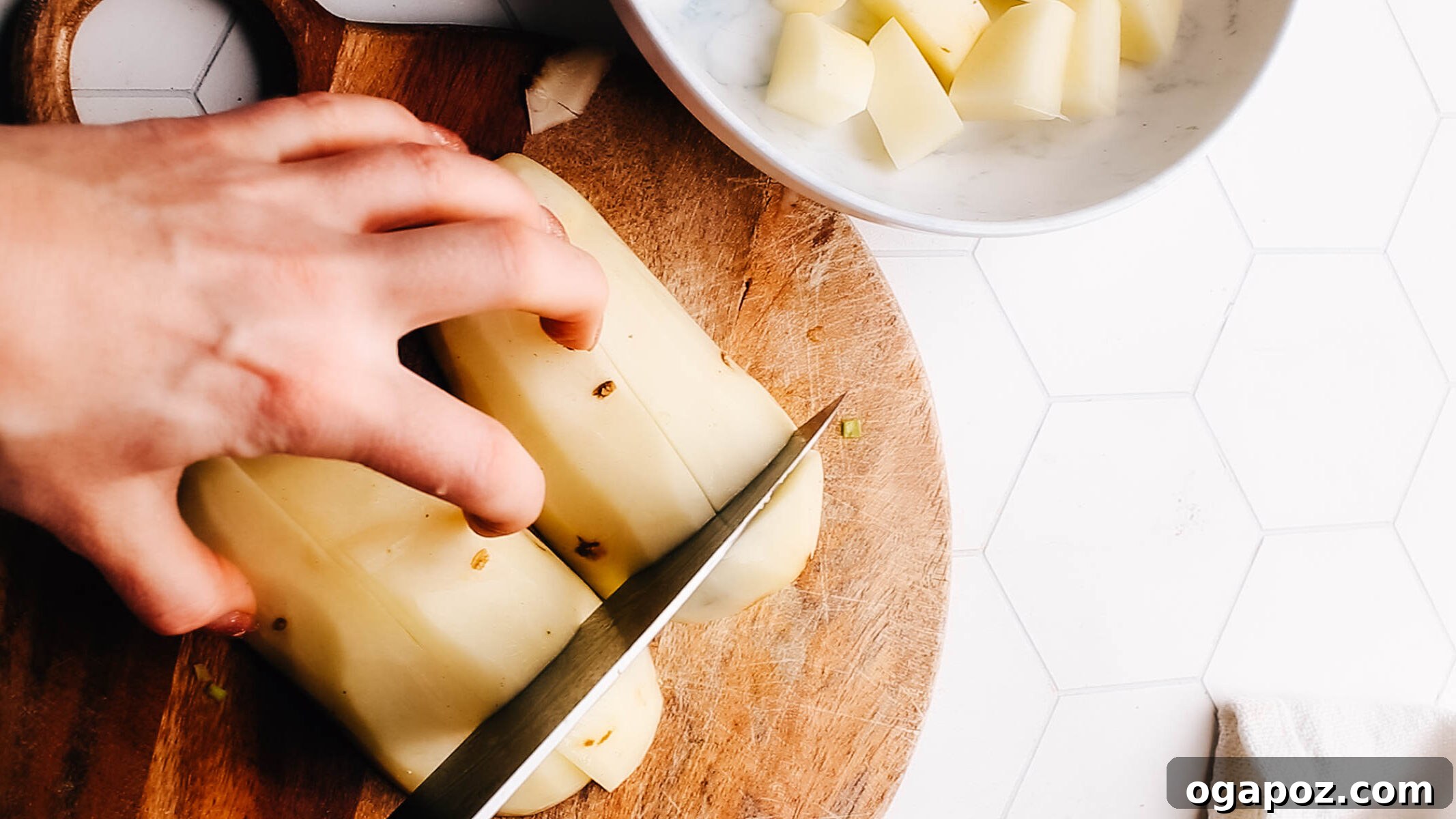 The Mashed Potato Recipe That Changes Everything 3 Fresh Russet potatoes being chopped on a wooden board, ready for cooking.