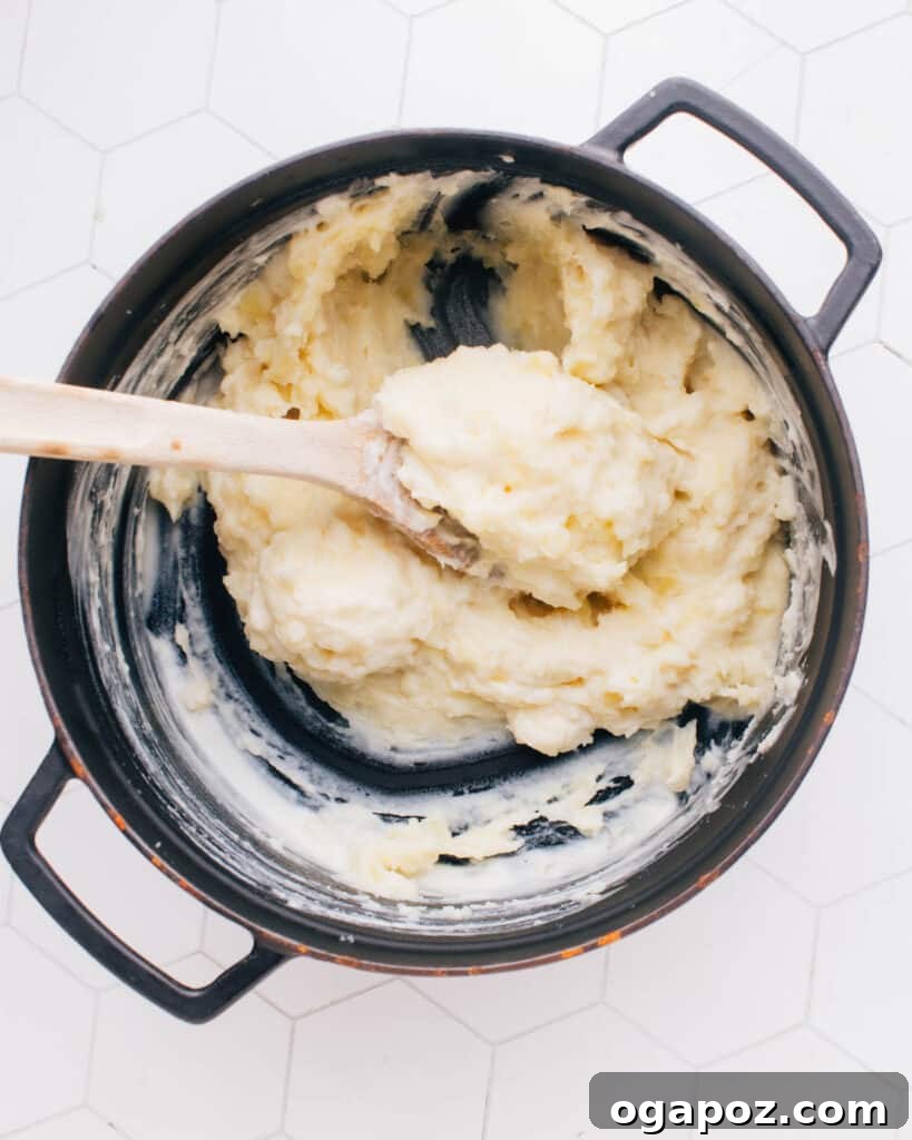 The Mashed Potato Recipe That Changes Everything 9 The mashed potatoes are being gently stirred with a spatula, creating a smooth and creamy consistency after the warm dairy has been incorporated.