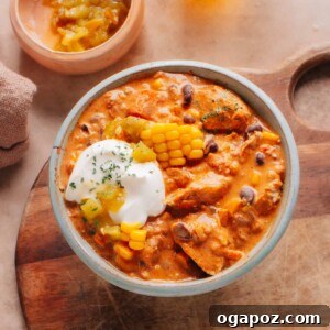 The ultimate creamy Cream Cheese Chicken Chili in a bowl, generously topped with fresh corn, green chilies, and a swirl of cream cheese, capturing its inviting richness.