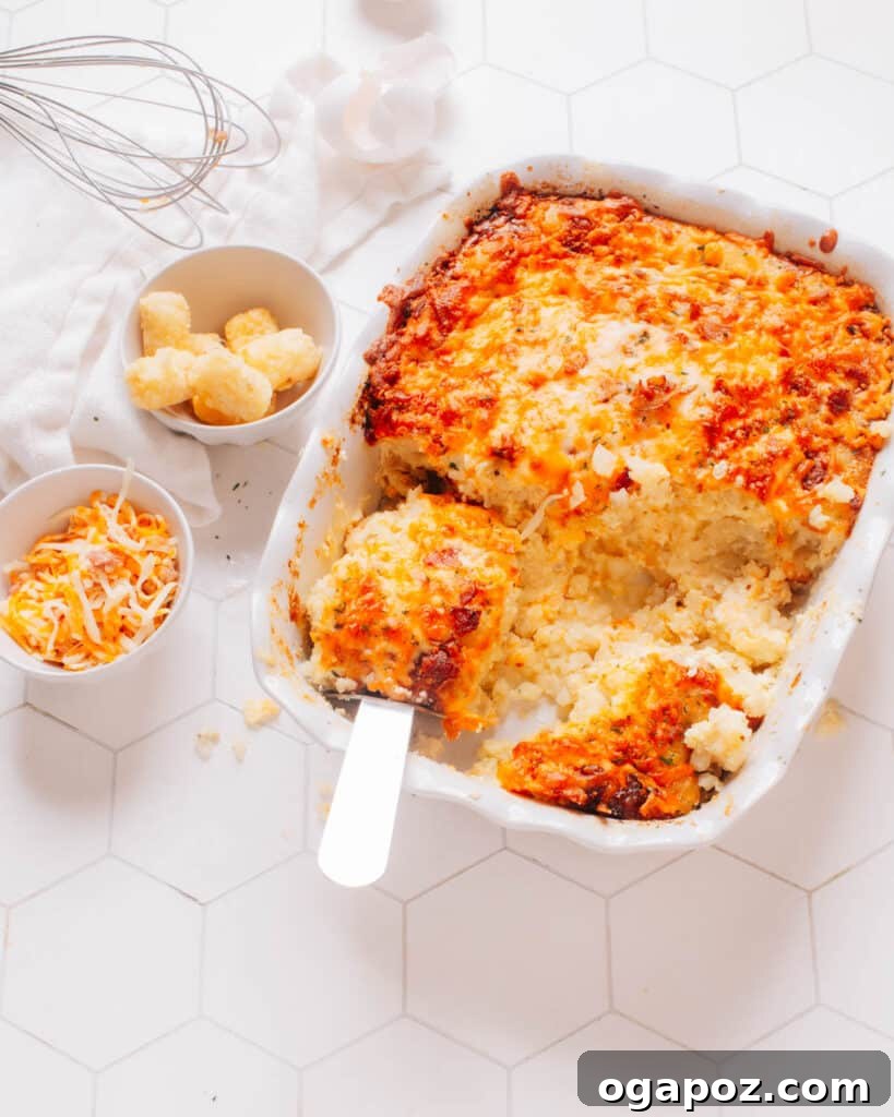 Golden Tater Tot Morning Bake 2 Tater Tot Breakfast Casserole in a baking dish with a serving spoon lifting out a piece.