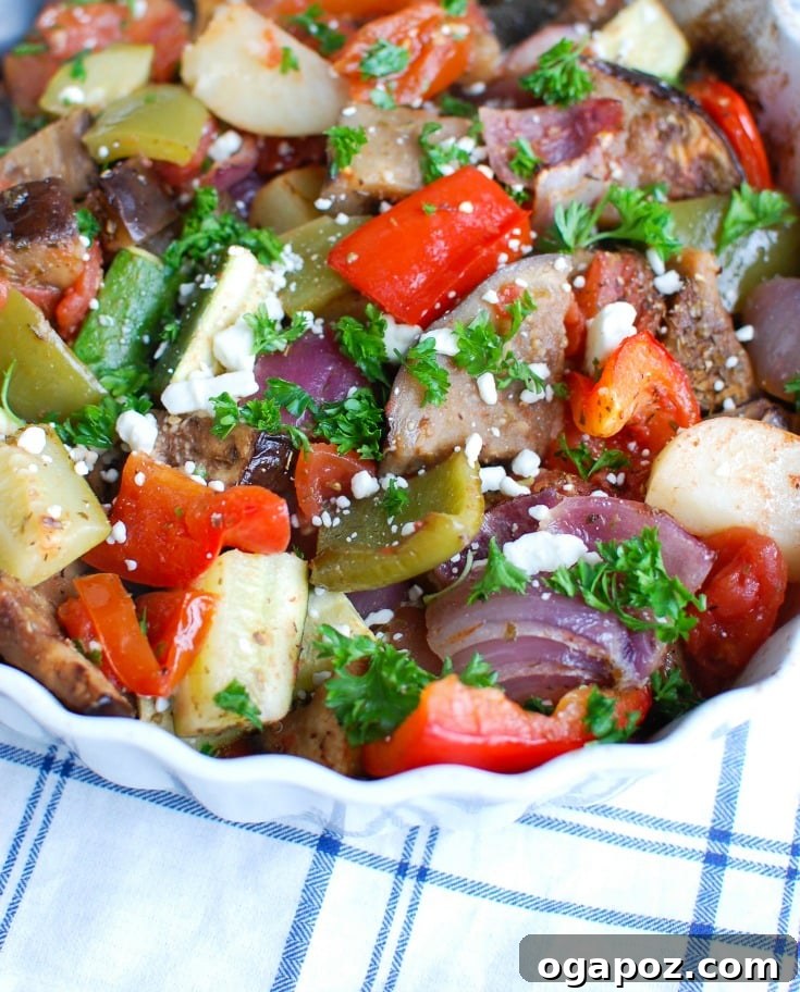 Close-up shot of raw, sliced Greek vegetables including zucchini, eggplant, potatoes, bell peppers, and tomatoes, mixed with herbs and olive oil, ready for roasting in a baking dish.