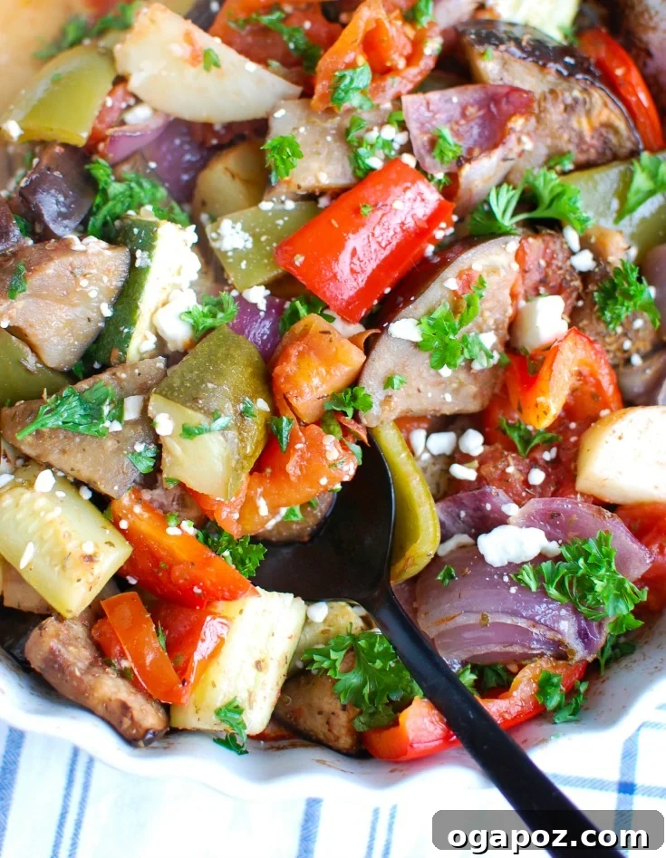 Plated Greek Roasted Vegetables (Briami) garnished with fresh parsley and crumbled feta, served alongside a spoon, highlighting the delicious textures and vibrant colors.