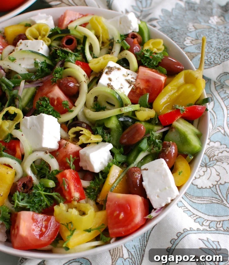 Spiralized Greek Style Salad in a white bowl, garnished with fresh herbs