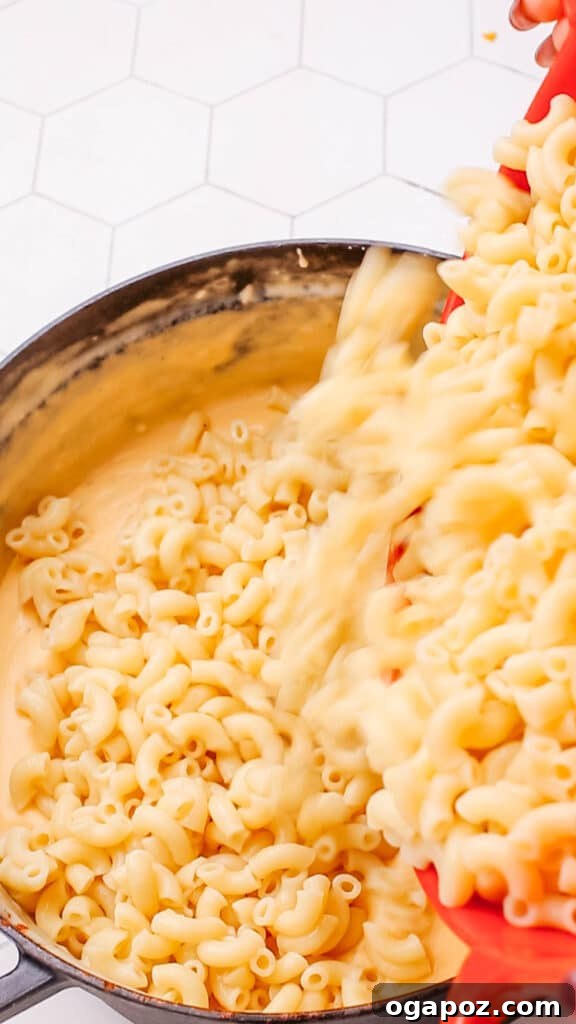 Classic Velvety Baked Macaroni and Cheese 12 Cooked macaroni pasta being mixed into a large pot of creamy cheese sauce.