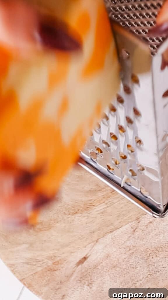 Classic Velvety Baked Macaroni and Cheese 6 Hands grating fresh cheese over a bowl, highlighting the importance of freshly shredded cheese for the recipe.