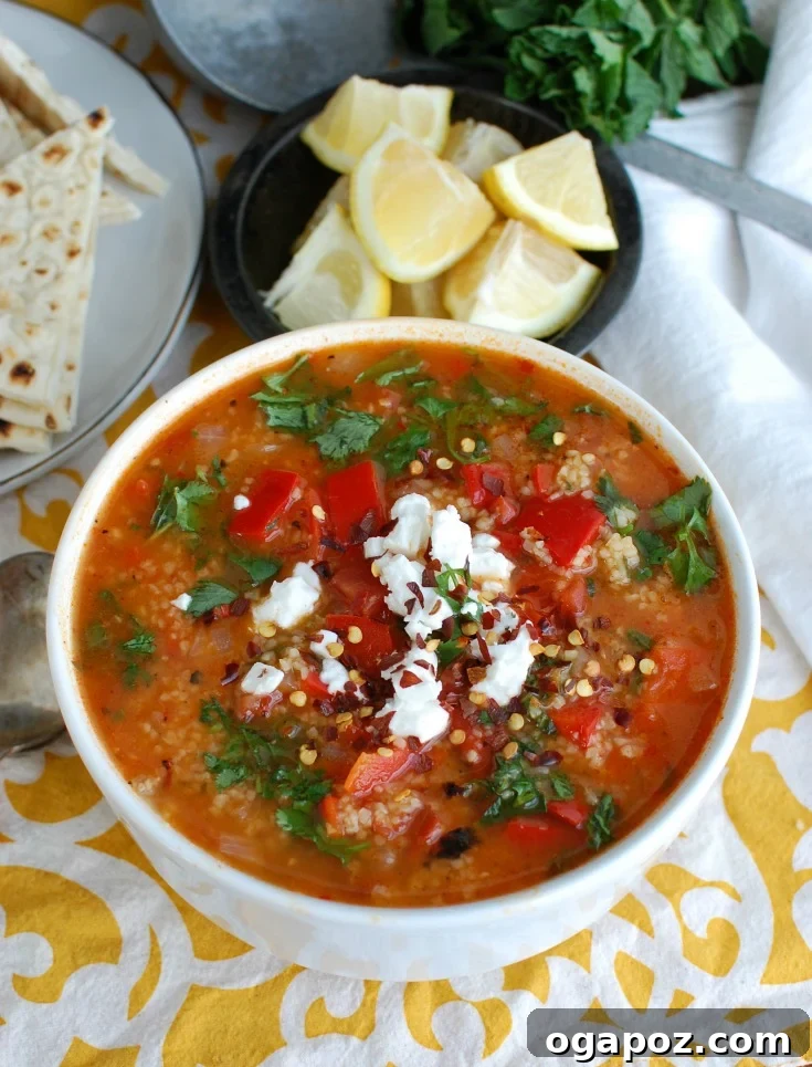 Hearty Tomato and Red Pepper Bulgur Soup 3 A close-up of Tomato Red Pepper Bulgur Soup garnished with crumbled feta cheese and fresh herbs, invitingly presented.