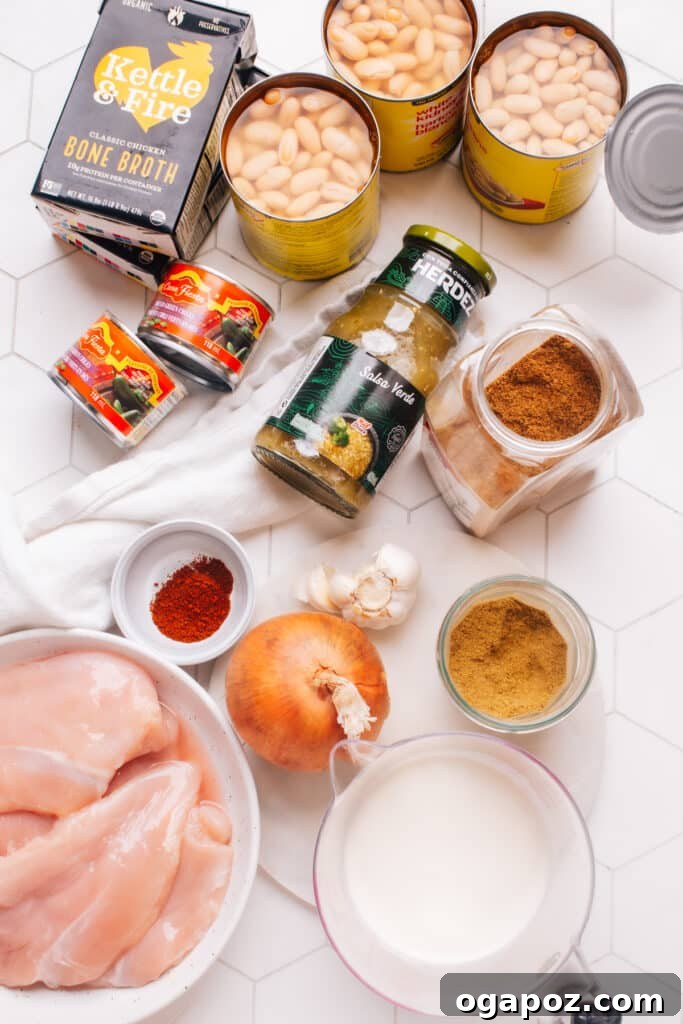 Wholesome White Chicken Chili 3 All the fresh ingredients for a healthy white chicken chili laid out on a wooden board, including chicken breasts, onions, garlic, various spices, canned beans, green chilies, milk, and fresh lime.
