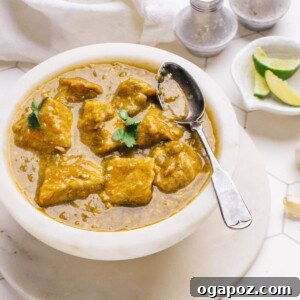 Chile verde in a bowl with a spoon, garnished with fresh herbs.