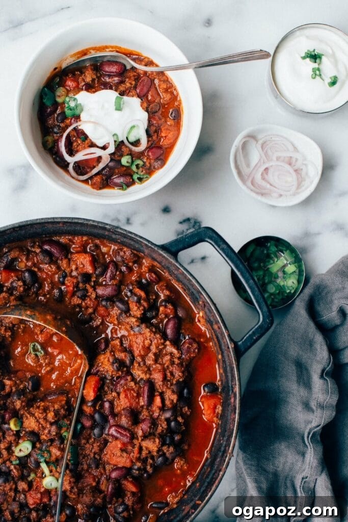 Secret Chili Seasoning Recipe 7 A bubbling pot of hearty ground beef chili, with a serving bowl of chili garnished with fresh herbs placed invitingly beside it.