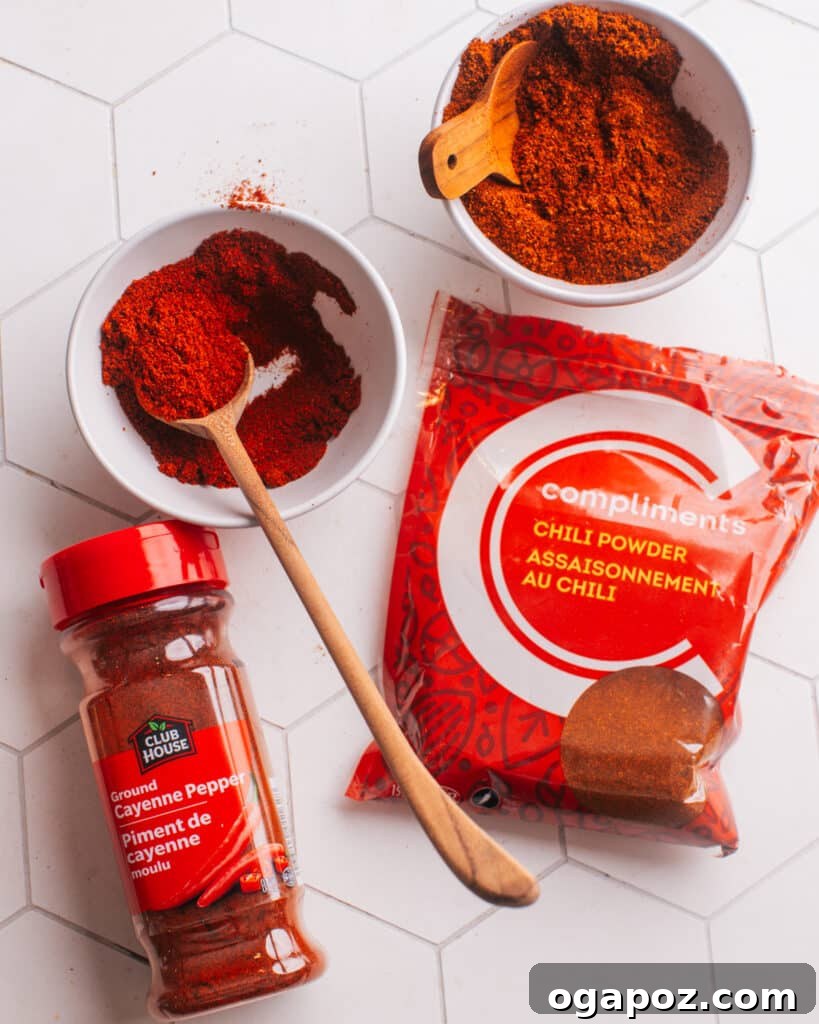 Secret Chili Seasoning Recipe 9 Two distinct piles of spice—one of bright orange cayenne pepper and one of rich red chili powder—placed side-by-side for comparison on a white surface.