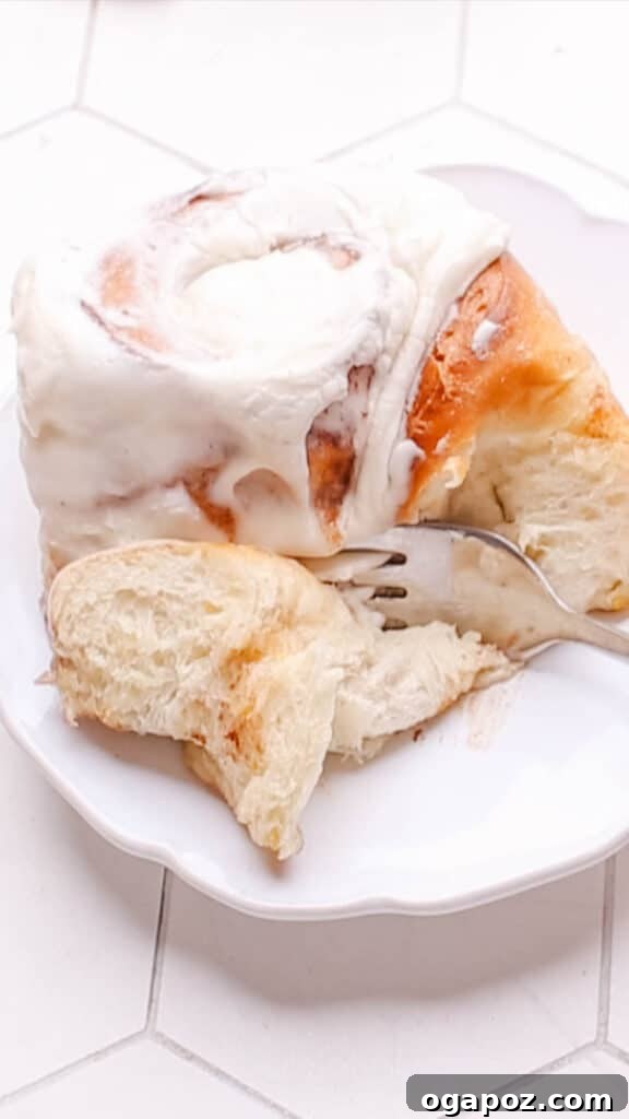 Sweet Cinnamon Swirls with Raisins 3 Close-up of a fork cutting into a soft, frosted cinnamon raisin roll, revealing its gooey interior.