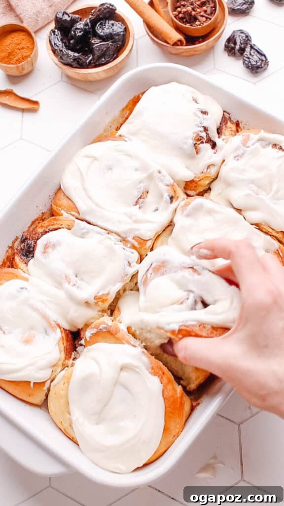 Sweet Cinnamon Swirls with Raisins 10 A hand pulling out a perfectly baked and frosted cinnamon raisin roll from a pan, ready to be enjoyed.