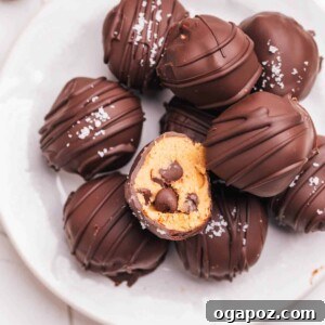 Effortless Cookie Dough Bites 16 A pile of chocolate-covered cookie dough bites on a plate, with one bite taken from the top one.