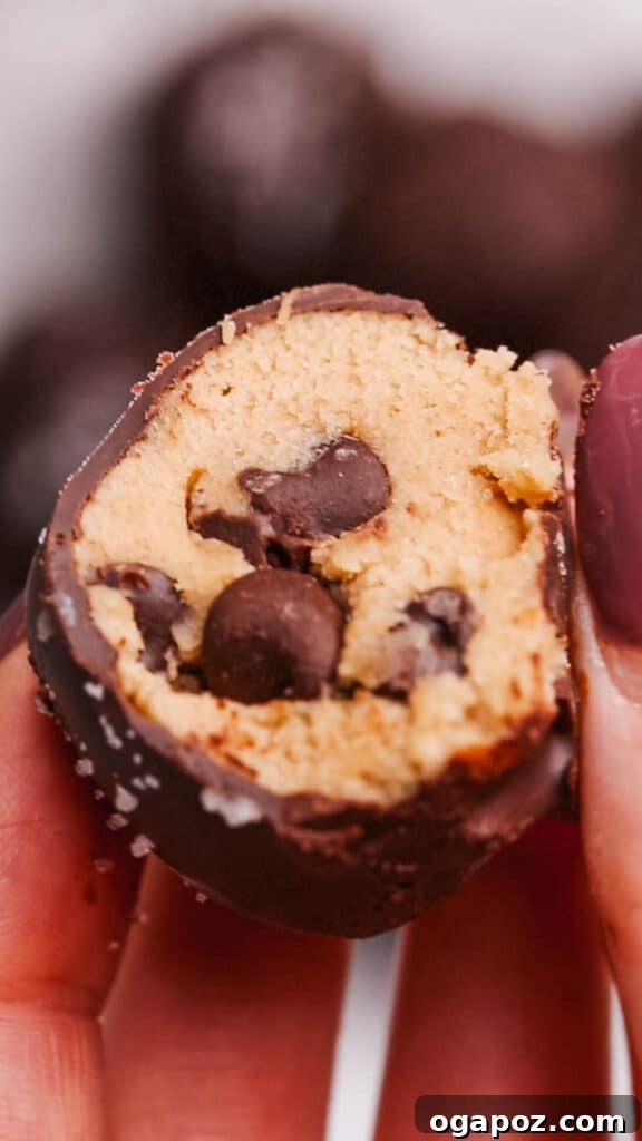 Effortless Cookie Dough Bites 3 A close up shot of the inside of a chocolate-coated cookie dough bite, showing its soft texture and chocolate chips.