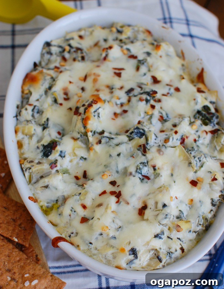 Zesty Lemon Artichoke Spinach Dip 2 Lemon Spinach Artichoke Dip served in a white bowl with a napkin and bread in the background