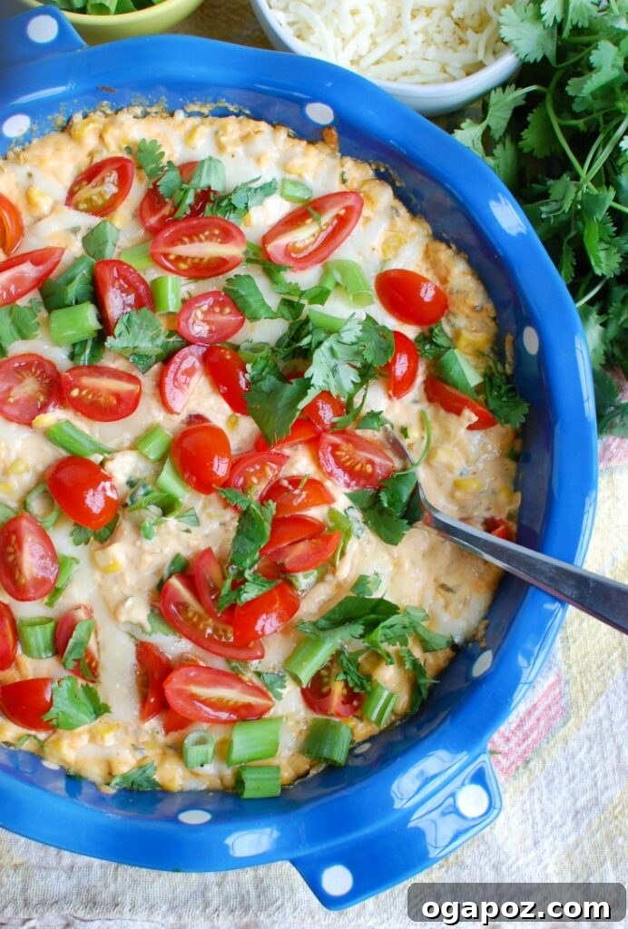 Baked Sriracha Sweet Corn Dip, garnished with fresh herbs and tomatoes, served with tortilla chips, inviting and vibrant