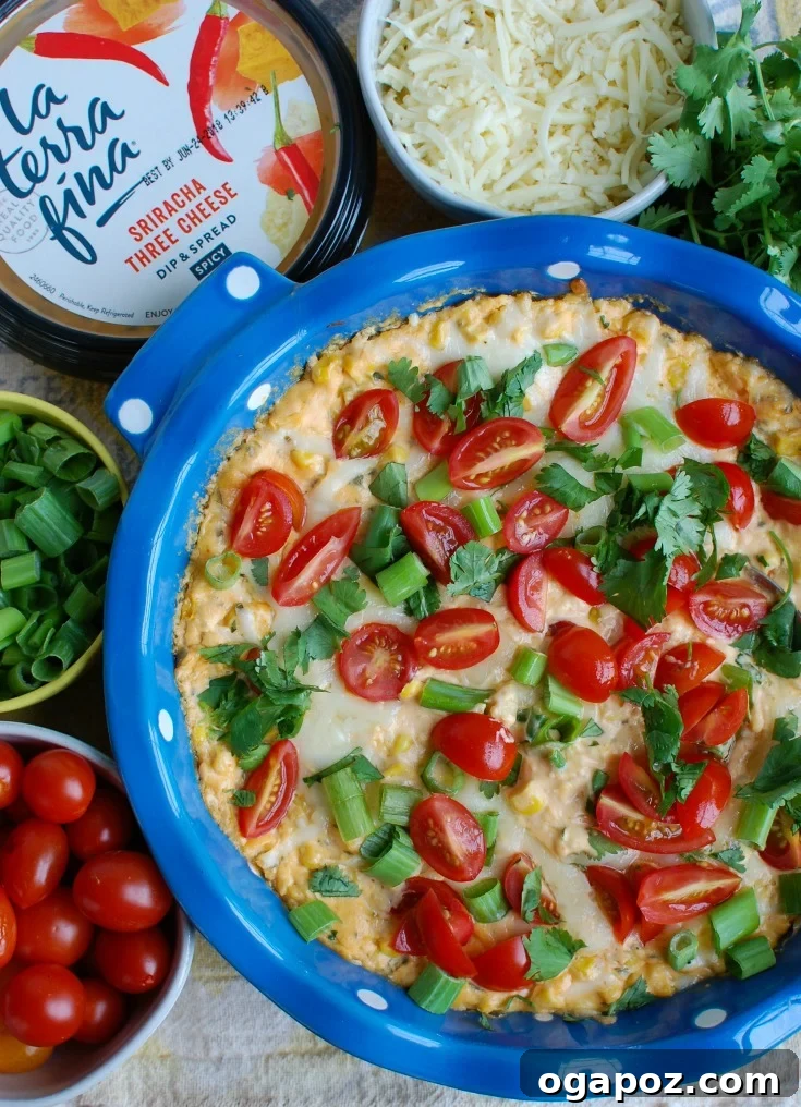 Baked Sriracha Sweet Corn Dip in a blue ceramic dish, with a spoon, highlighting its warm, cheesy texture