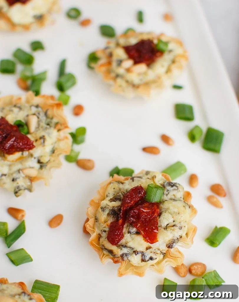 Savory Sun-Dried Tomato Spinach Artichoke Phyllo Bites 2 Spinach Artichoke Sun-dried Tomato Phyllo Bites on White Plate, garnished with fresh herbs.
