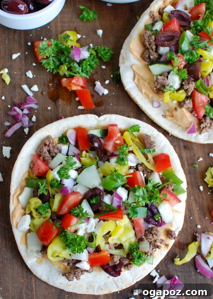 Greek-Style Beef Pita Pizza 4 Overhead view of a ready-to-eat Greek Beef Pita Pizza, generously topped with colorful ingredients and fresh herbs.