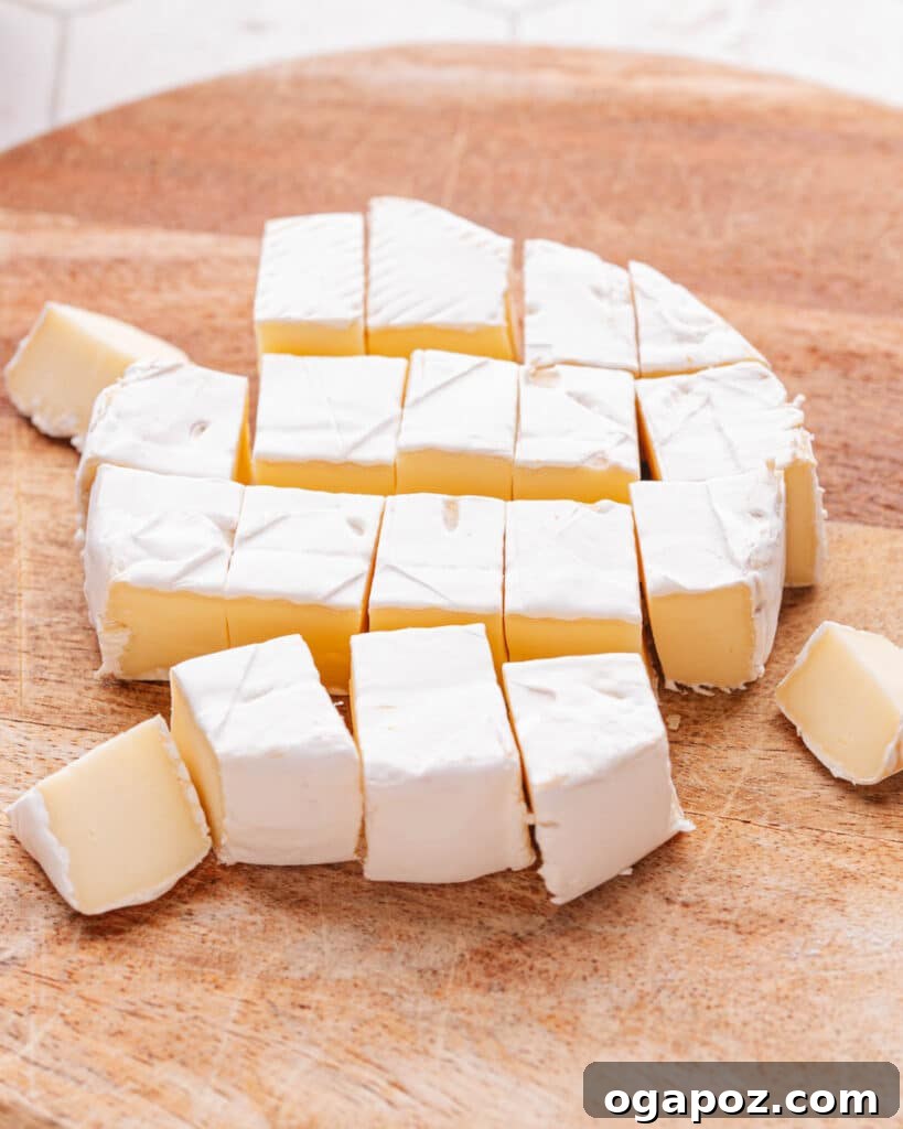 Effortless Brie Everyone Will Love 7 Small, uniformly cut pieces of brie cheese on a cutting board, ready for assembly.