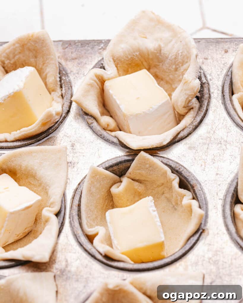Effortless Brie Everyone Will Love 8 Brie bites carefully placed in puff pastry in a mini muffin tin, ready for baking.