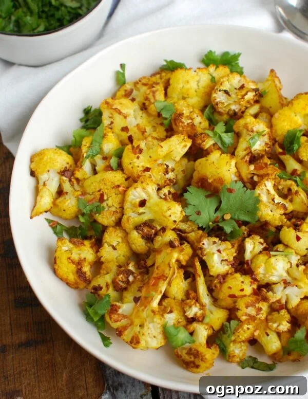 Golden Turmeric Roasted Cauliflower 3 Turmeric Roasted Cauliflower served in a white dish, garnished with fresh cilantro, highlighting its vibrant color.