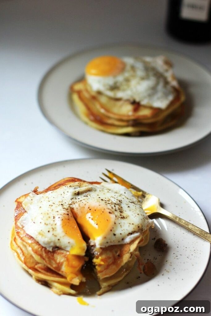 A towering stack of savory Sausage Pancakes with a perfectly fried, runny egg on top, creating an irresistible breakfast sensation.