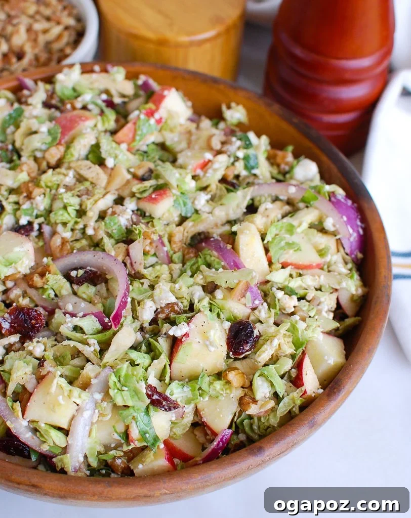 Harvest Brussels Salad with Apple & Chèvre 5 A wooden bowl filled with Brussels Sprout Apple Goat Cheese Salad, with wooden tongs resting on the side, ready to serve.