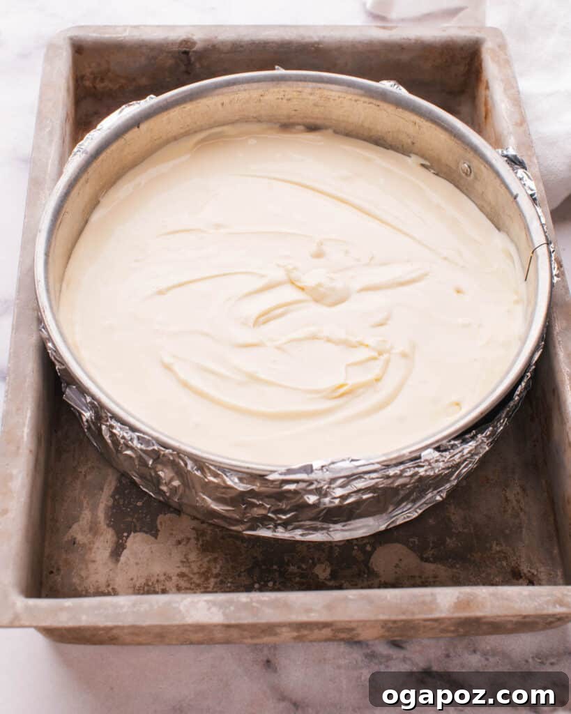 Philadelphia Cheesecake Classic Perfection Pro Insights 14 A springform pan with cheesecake batter, wrapped in foil and placed in a larger roasting pan filled with water for a water bath.