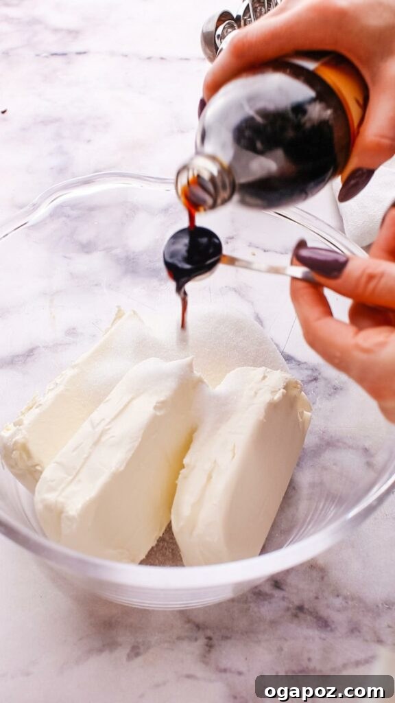 Philadelphia Cheesecake Classic Perfection Pro Insights 6 A hand adding a liquid ingredient, possibly vanilla extract, into a bowl of Philadelphia cream cheese mixture.