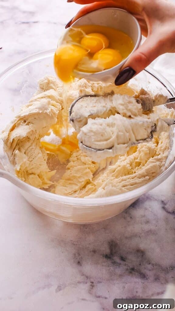 Philadelphia Cheesecake Classic Perfection Pro Insights 8 A hand cracking an egg into a bowl of creamy Philadelphia cream cheese and sugar mixture.