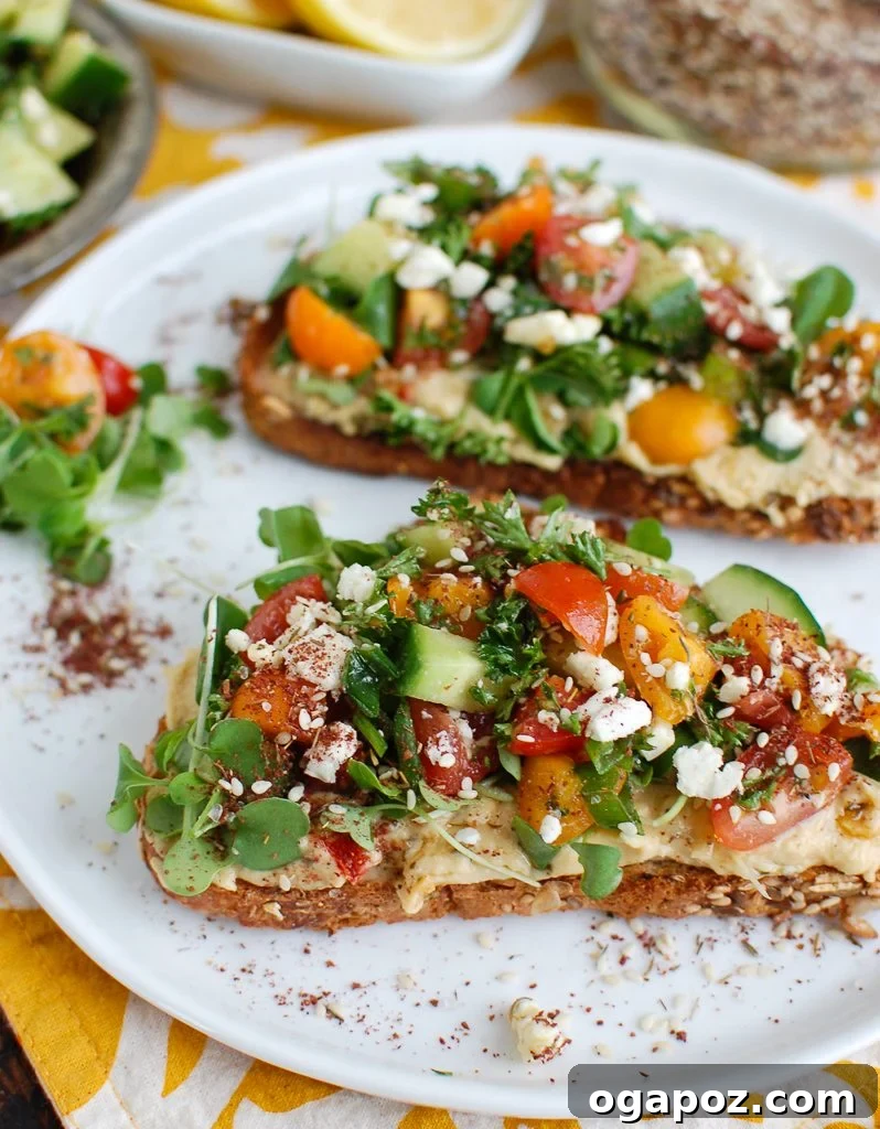 Savory Mediterranean Hummus Toast with Za'atar Two slices of Mediterranean Hummus Toast with Za'atar, topped with fresh ingredients like tomatoes, cucumbers, and feta.